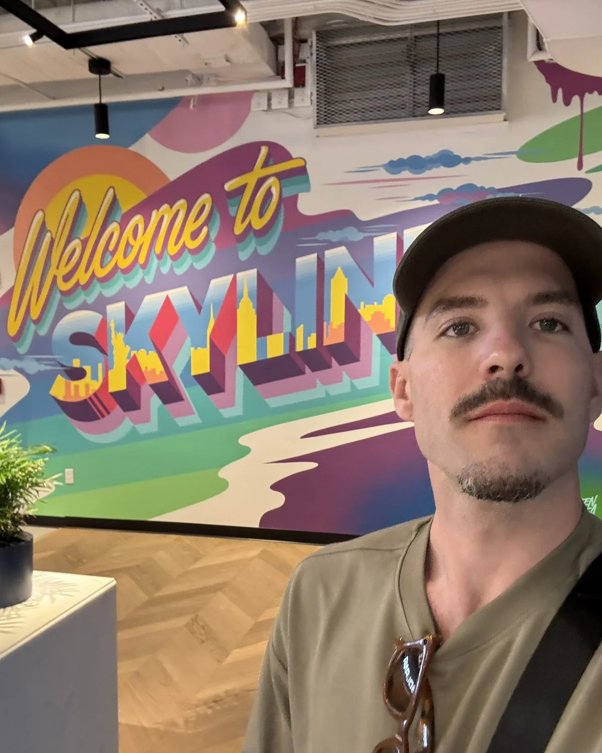 Matthew Karsten in front of a Welcome to Skyline mural in New York.